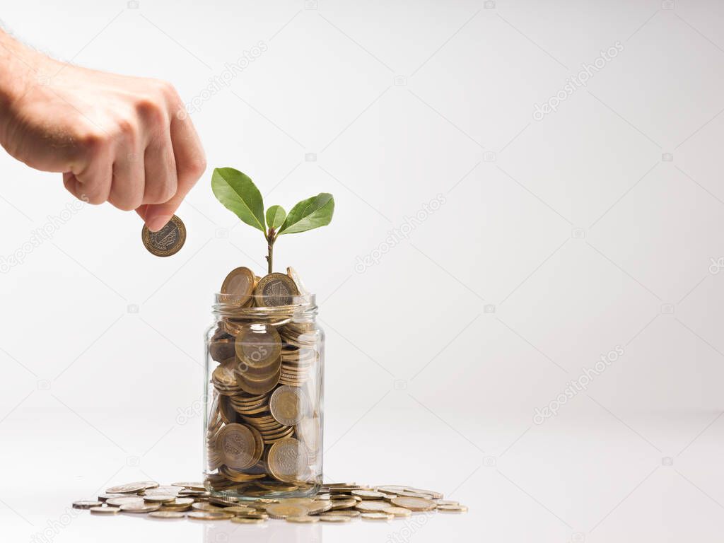 Hand of person holding coin to put in glass jar. Turkish coins in jars. Plants in jar and Turkish 1 TL coins Savings and Finance concept.
