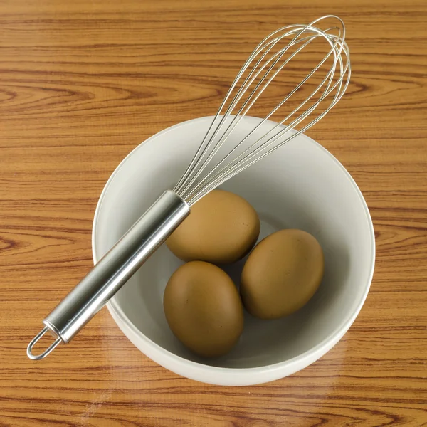 Whisk and egg in white bowl — Stock Photo, Image
