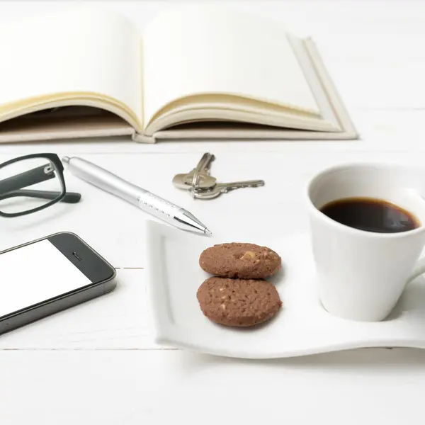 Xícara de café com biscoito, telefone, caderno aberto, chave e óculos — Fotografia de Stock