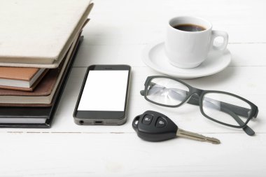 kahve fincanı ile telefon, araba anahtarı, gözlük ve kitap yığını