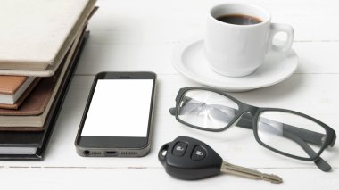 kahve fincanı ile telefon, araba anahtarı, gözlük ve kitap yığını