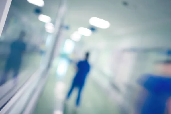 Blurred figures of medical doctors walking in the long hospital corridor, defocused background.