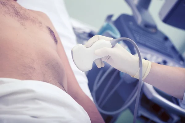 Doctor performs the ultrasonic diagnostic to the male patient in the hospital.