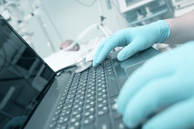 Doktor yoğun bakımda dizüstü bilgisayarda yazarak