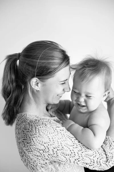 young mom laughs and hugs her son, baby 1 year old, baby care leave, happy motherhood and childhood, black and white photo, selective focus