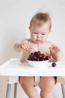 Bebek sandalyeye oturur ve kirazları, olgun meyvelerin içindeki doğal vitaminleri, çocuk koltuğundaki bir çocuğun portresini yer.