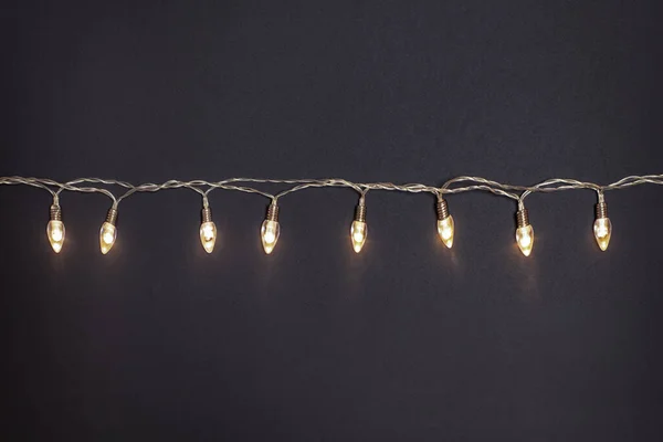 a garland of retro light bulbs is burning with warm yellow light on a black background,