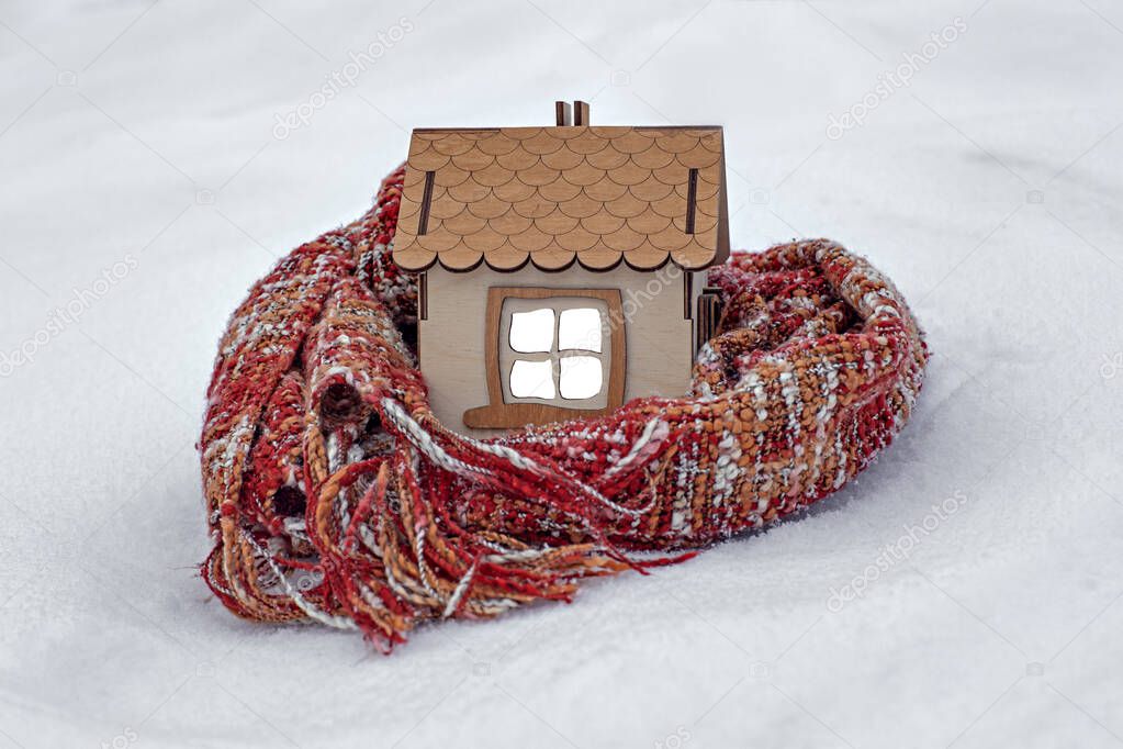 a wooden house in the snow in winter, a knitted scarf around the house, the concept of insulation and heating, protection of the house from winter cold,