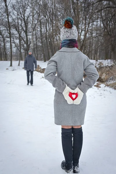 女性の手に赤いハート冬の公園を散歩中のカップルバレンタインデーの驚き2月14日の背景 — ストック写真