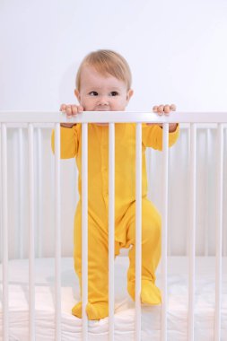 a baby in a yellow pajamas stands in a crib, a 10 month old baby woke up in the morning, baby safety clipart