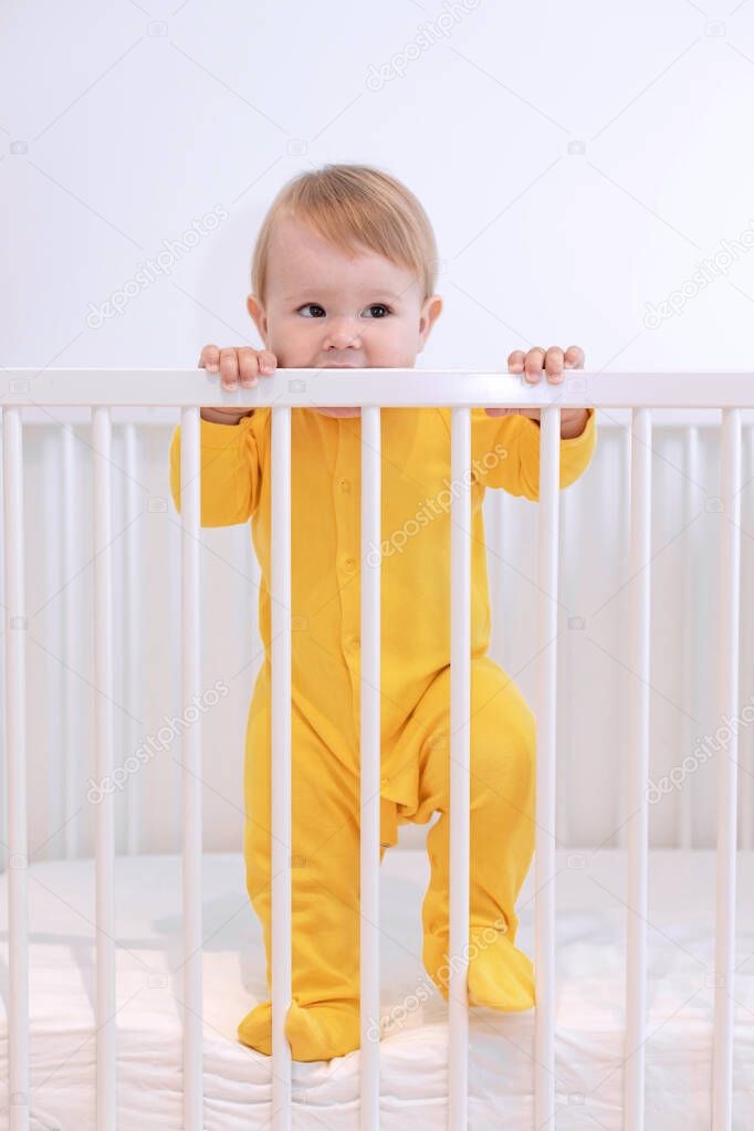 a baby in a yellow pajamas stands in a crib, a 10 month old baby woke up in the morning, baby safety