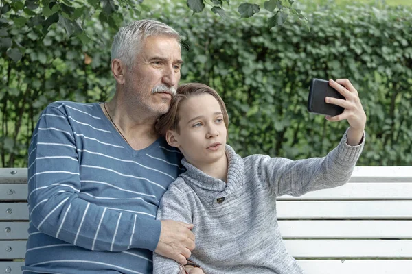 grandson and grandfather  take a selfie on a park bench, take a photo on the phone for memory, family together