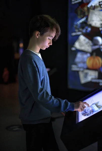 A boy uses an interactive touchscreen displayed in the museum. Education, technology and future concept.