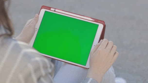 Een jonge vrouw zit buiten en werkt op een tablet — Stockvideo