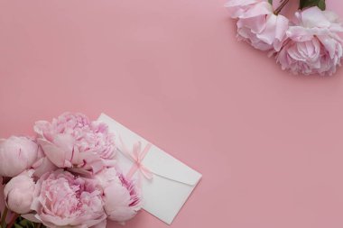 Şakayıklar pembe arka planda yatıyordu, güzel narin çiçekler ve beyaz bir zarf, bir etkinliğe davetiye, doğum günü, düğün, anneler günü konsepti