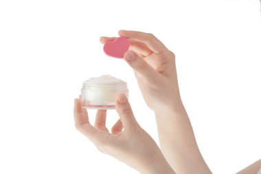 Beyaz arka planda nemlendirici, kadın elleri kozmetik ürünler, cilt bakımı, pembe kalp şeklinde sünger, cilde krem sür.