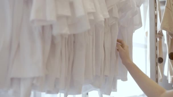 Beautiful womans hand goes over white T-shirts in the mall, shopping centre, High quality FullHD footage — Stock Video