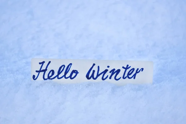 paper with hand lettering hello winter on a background of winter snow