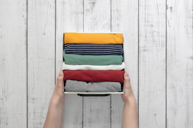 Elleri düzgünce katlanmış giysileri olan bir konteynırı tutar, eşyaları depolar, eşyaları dolaba koyar.