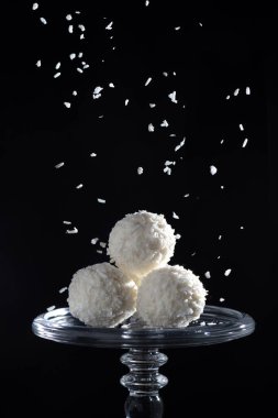 Hindistan cevizi taneleri serpiştirilmiş siyah bir zemin üzerinde yuvarlak hindistan cevizi şekeri, nefis bir lezzet, tatlı bir zevk, güzel bir stüdyo çekimi.