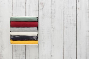 Eşyaları ahşap arka planda bir kabın içinde düzgünce katladı, kopyala alanı, düzeni koruma ve giysileri depolama konsepti