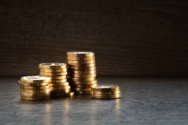 Koyu arkaplanda paralar, bir sürü sarı, altın paralar masanın üzerine istiflenmiş.