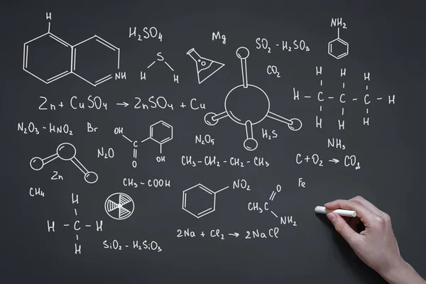 hand with chalk draws on the blackboard formulas and elements, signs and symbols of chemistry, the concept of the study of substances, organic chemistry