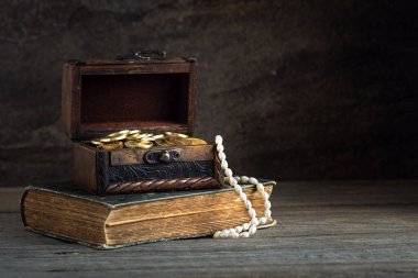 Sandık altın sikkelerle ahşap bir masada eski bir kitap, eski tarz, zenginlik konsepti, korsan hazinesi, açgözlülük