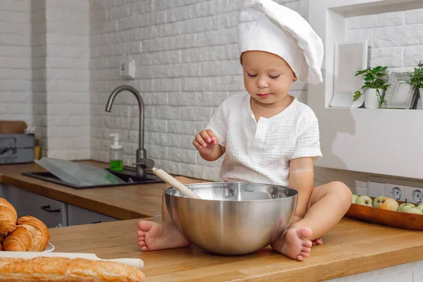 kid in the kitchen wearing a white chef\'s hat, child playing with kitchen utensils, mother\'s little helper, delicious family recipes concept