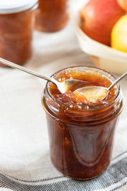 Ev yapımı elma reçeli marmelatlı karanfil ve şeffaf cam bir kavanozda organik elmalardan elde edilen tarçınlı reçel reçeli ve antika bir kaşık. Ev yapımı sonbahar reçeli.