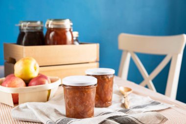 Ahşap kaşığın yanında şeffaf bir bardakta organik elmalardan elde edilen karanfil ve tarçınlı ev yapımı elma reçeli reçeli. Ev yapımı sonbahar reçeli konserveleri.