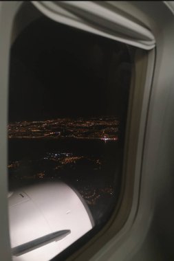 Şehir ışıkları gece uçağın tepesinden penceredeki gökyüzünden görünüyor. 