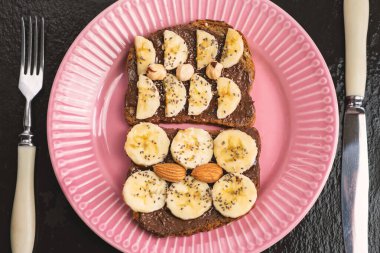 Kızarmış tam buğday ekmeği, çikolatalı fındık ezmeli fındık ezmesi, muz, chia tohumu, badem ve fındıklı tost. Kahvaltı için sağlıklı beslenme
