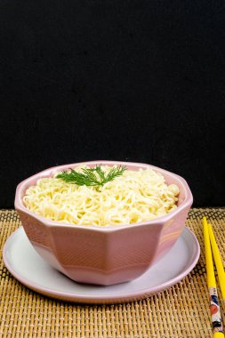 Pembe bir kasede maydanozlu hazır şehriye, gri masa örtüsü, Asya Çin ramen makarnası sarı bambu çubuklarıyla yenen fast food.