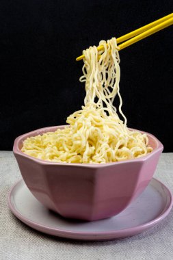 Siyah arka planda pembe bir kasede hazır şehriye, Asya Çin erişteli makarna sarı bambu çubuklarıyla yenen fast food.