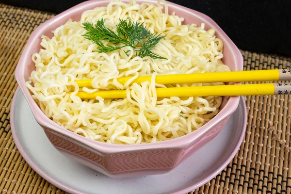 在灰色桌布上的粉红碗里放着欧芹的方便面 用黄竹筷子吃着亚洲拉面快餐 — 图库照片
