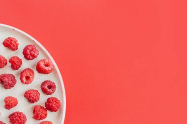 Olgun organik ahududu tabakta, sağlıklı yaz meyveleri üst manzara. Kırmızı arkaplanda kırmızı ahududu deseni düz..