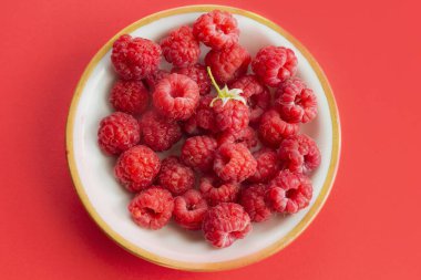 Olgun organik ahududu tabakta, sağlıklı yaz meyveleri üst manzara. Kırmızı arkaplanda kırmızı ahududu deseni düz..