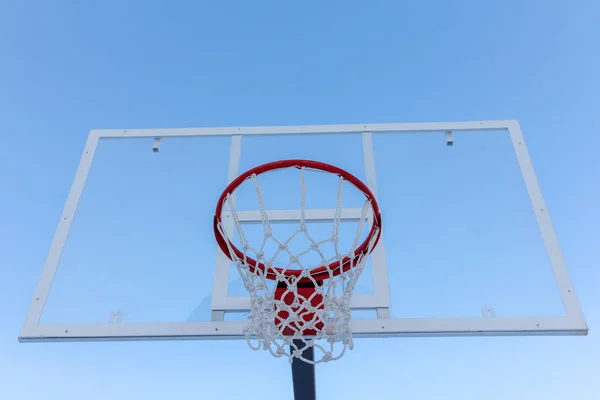 Street sports. Sports equipment on the street. Street basketball ring. Basketball board with basket hoop against blue sky.