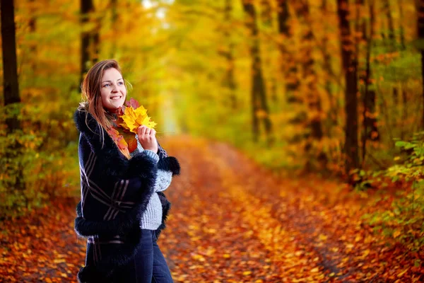 Девушка с листьями в руках в осеннем лесу позирует перед камерой. — стоковое фото