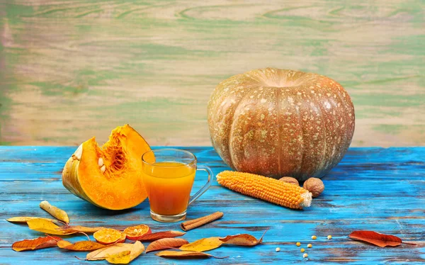 Ahşap mavi arka planda balkabağı suyu ve olgun meyve. Stüdyoda hala hayat var.