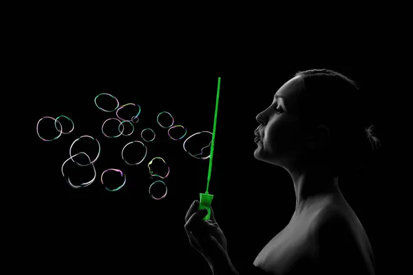 Junges Mädchen bläst Seifenblasen auf schwarzem Hintergrund — Stockfoto