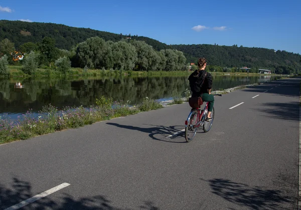 Passeios de ciclista ao longo da estrada de asfalto ao longo do rio — Fotografia de Stock