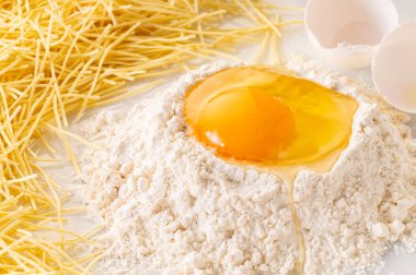 Un ve makarna içinde kırılmış yumurta, erişte yapmak için malzemeler.