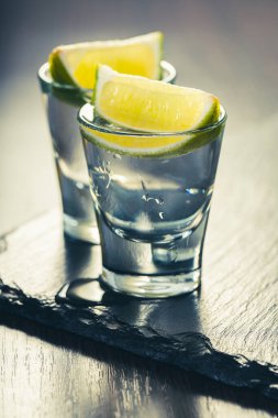 Koyu ahşap arka planda limonlu bardakta alkollü içecek.