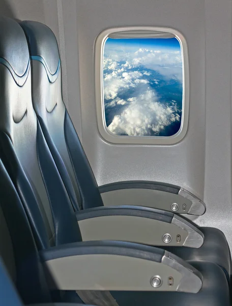 Zitplaatsen en venster binnen een vliegtuig met uitzicht op de blauwe lucht en de wolken — Stockfoto