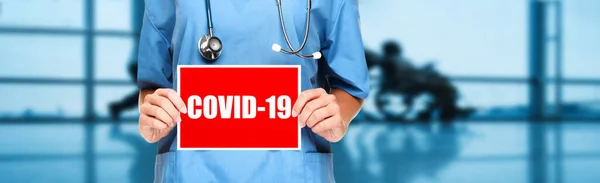 COVID-19 Coronavirus medic care deține semn în fundal banner spital. Lucrător medical panoramic care prezintă semnul panoramic al virusului corona cu titlu text — Fotografie, imagine de stoc