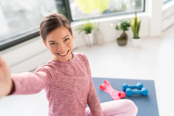 Feliz selfie en casa Asiática joven mujer sonriente entrenamiento peso corporal ejercicios en la esterilla de ejercicio en la sala de estar del apartamento tomando foto del teléfono móvil durante el entrenamiento —  Fotos de Stock