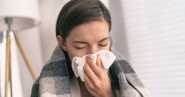 Cough in tissue covering nose and mouth when coughing as COVID-19 hygiene guidelines for coronavirus spread prevention. Asian woman sick with flu at home clipart