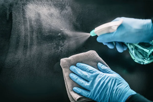 Pulizia della casa di superficie spruzzatura antibatterico igienizzante bottiglia spray disinfezione contro COVID-19 diffusione indossando guanti blu medici. Sanificare la prevenzione delle superfici negli ospedali e negli spazi pubblici — Foto Stock